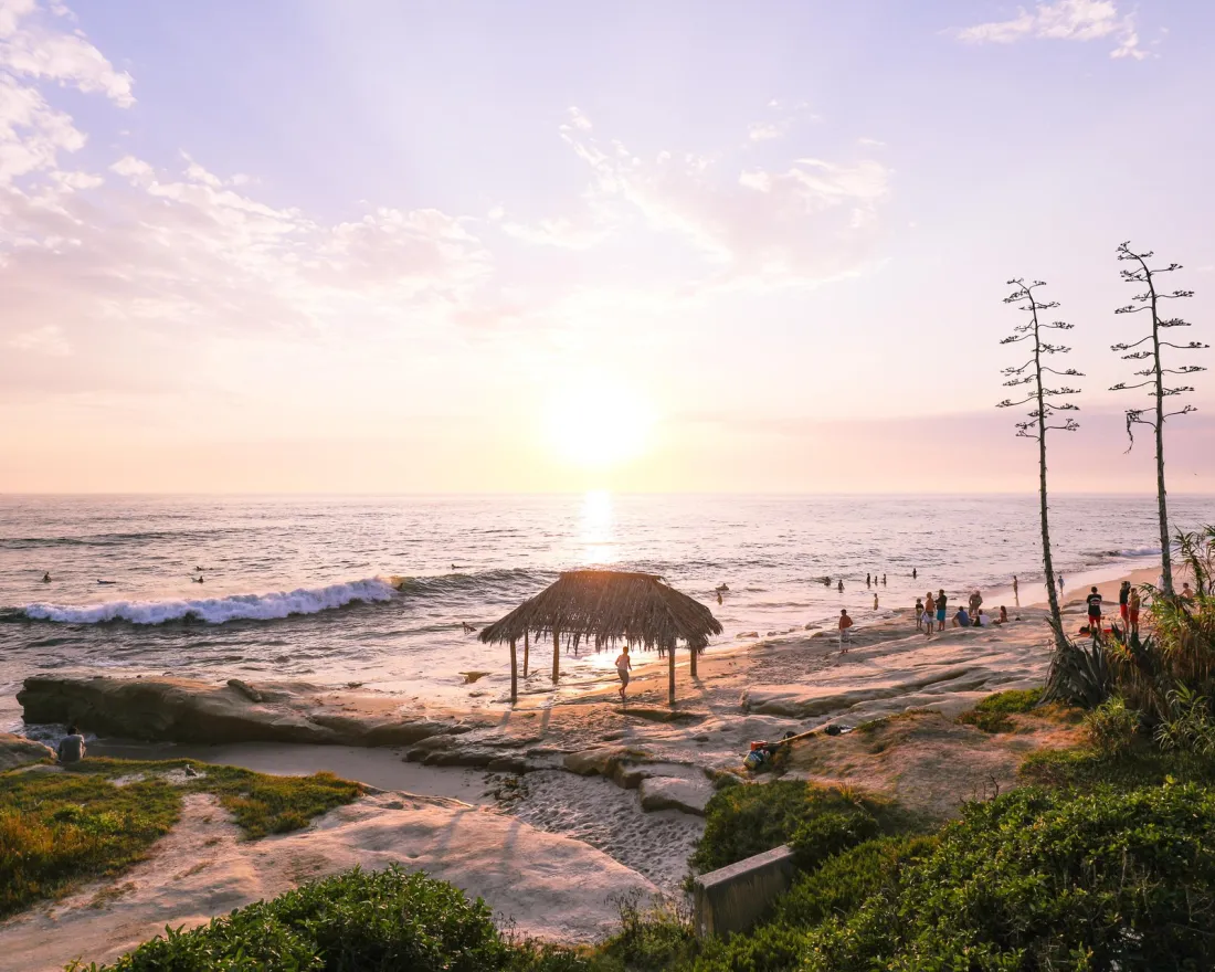 Sunset over the Windansea Beach in San Diego with a straw hut and people enjoying the waves.