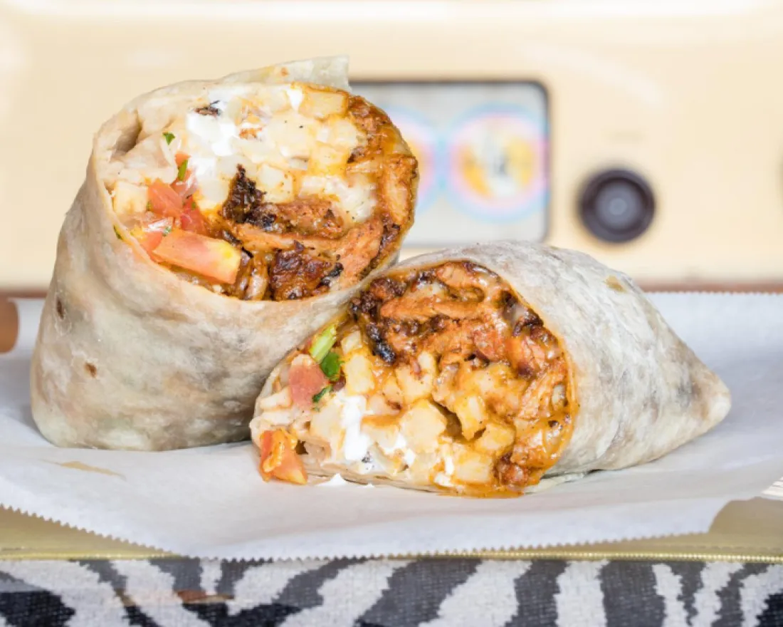 Two grilled burritos with fillings of carne asada, cheese, and pico de gallo on a striped surface.
