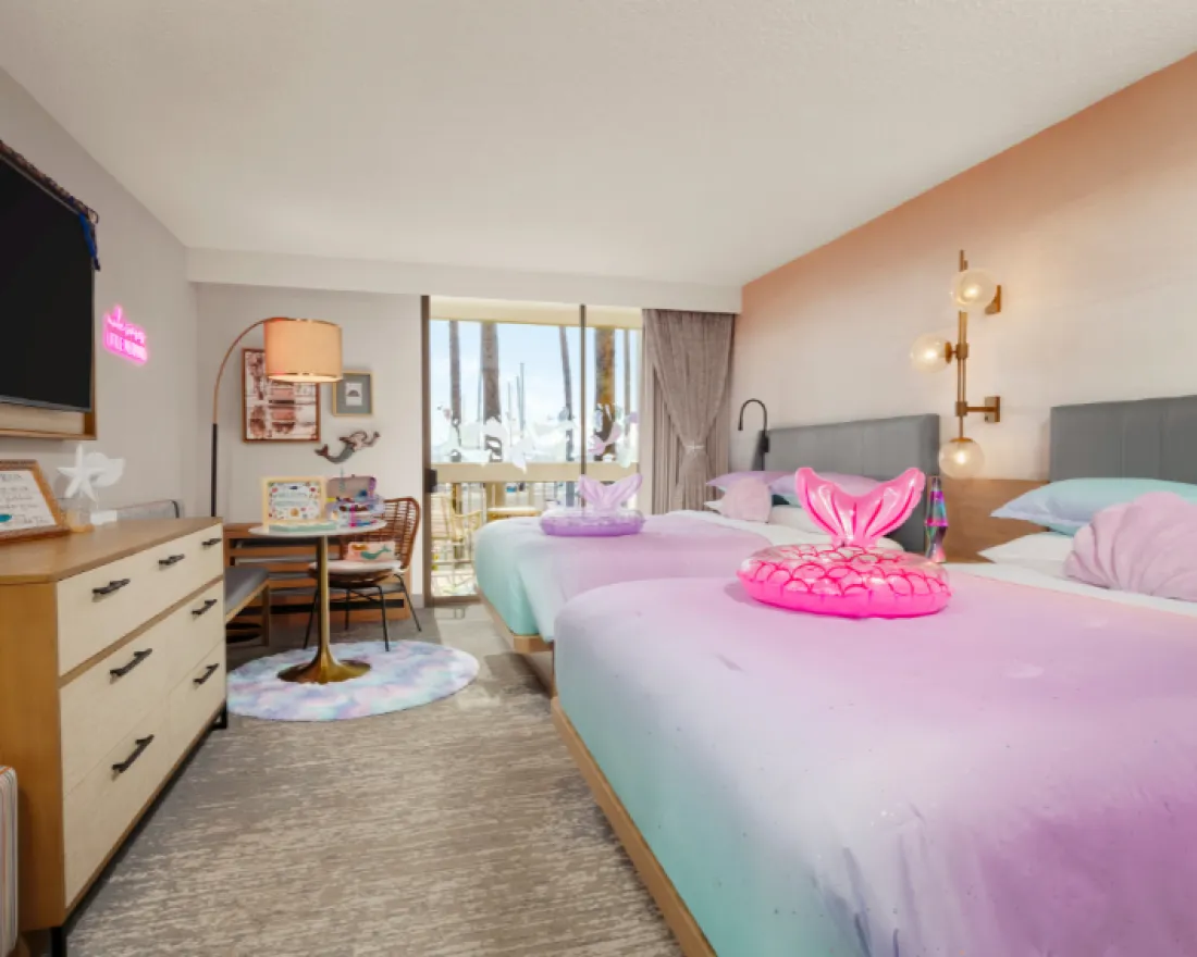 Colorful hotel room with two beds, a dresser, and a view of the balcony.