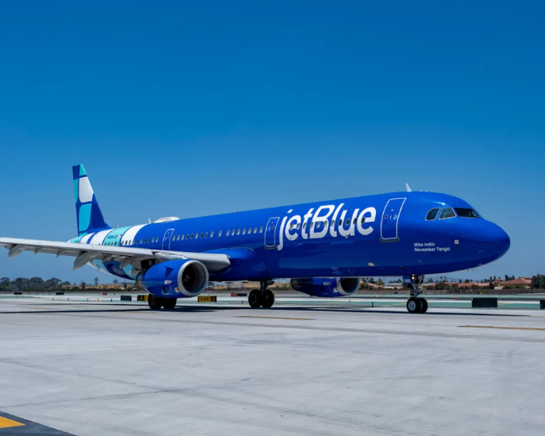 JetBlue airplane on runway under a clear blue sky.