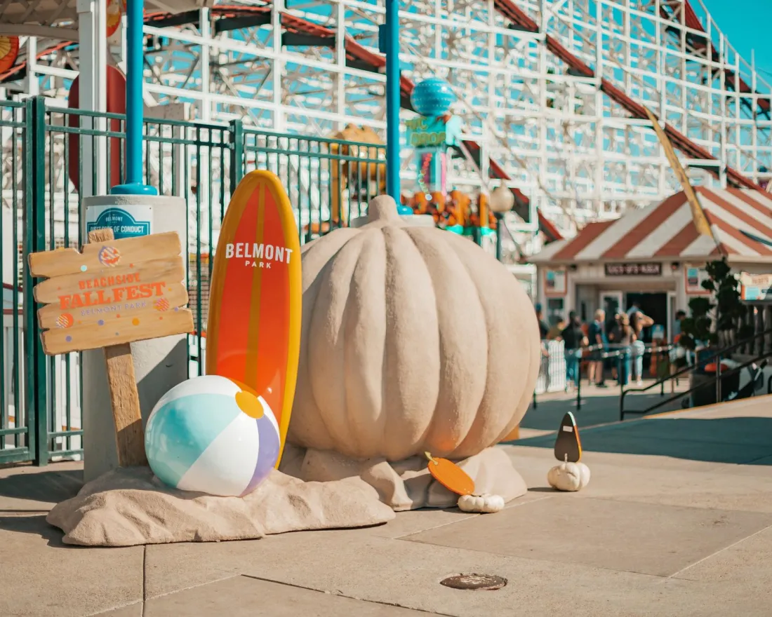 A large sand sculpture of a pumpkin with a beach ball and surfboards during the Beachside Fall Fest at Belmont Park in San Diego.
