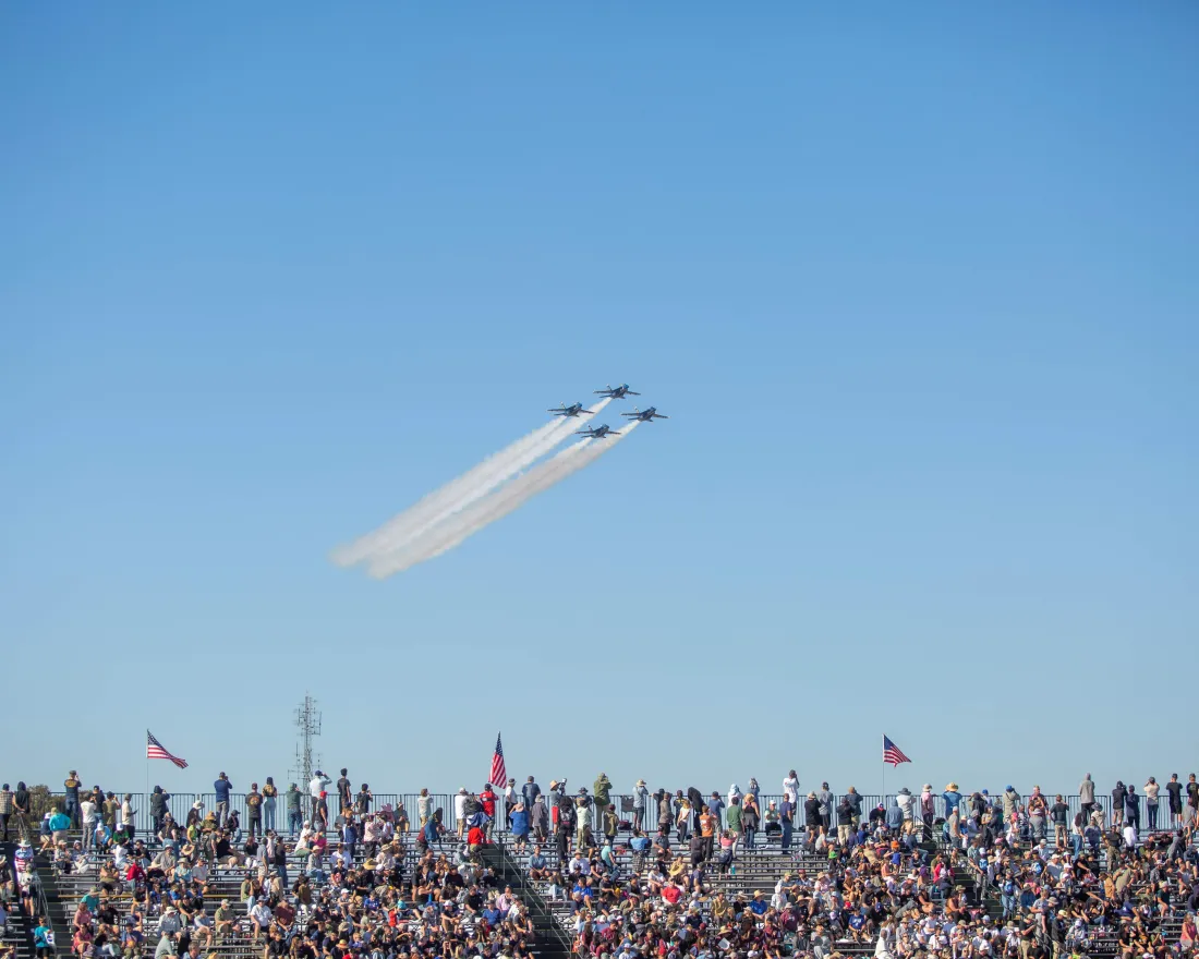 Three military fighter jets fly in formation, leaving vapor trails, above a large crowd at the MCAS Miramar Air Show in San Diego..