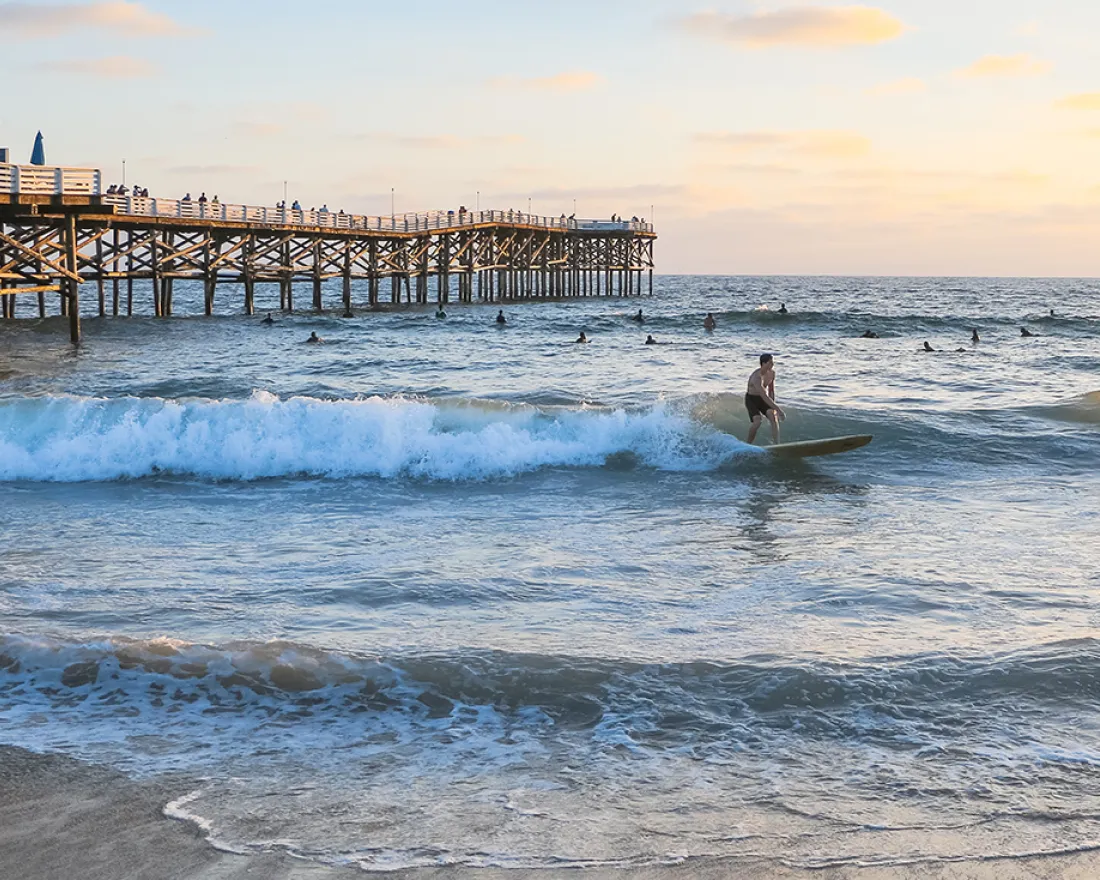 People swimming and surfing alongside Crystal Pier in Pacific Beach, San Diego, CA at sunset