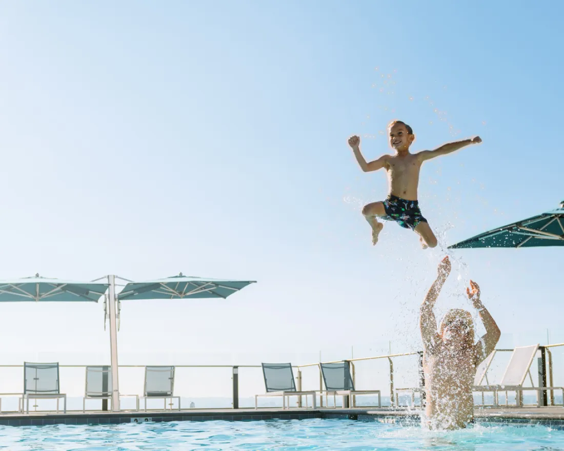 Kid jumps into mans arms splashing on rooftop pool in San Diego, CA