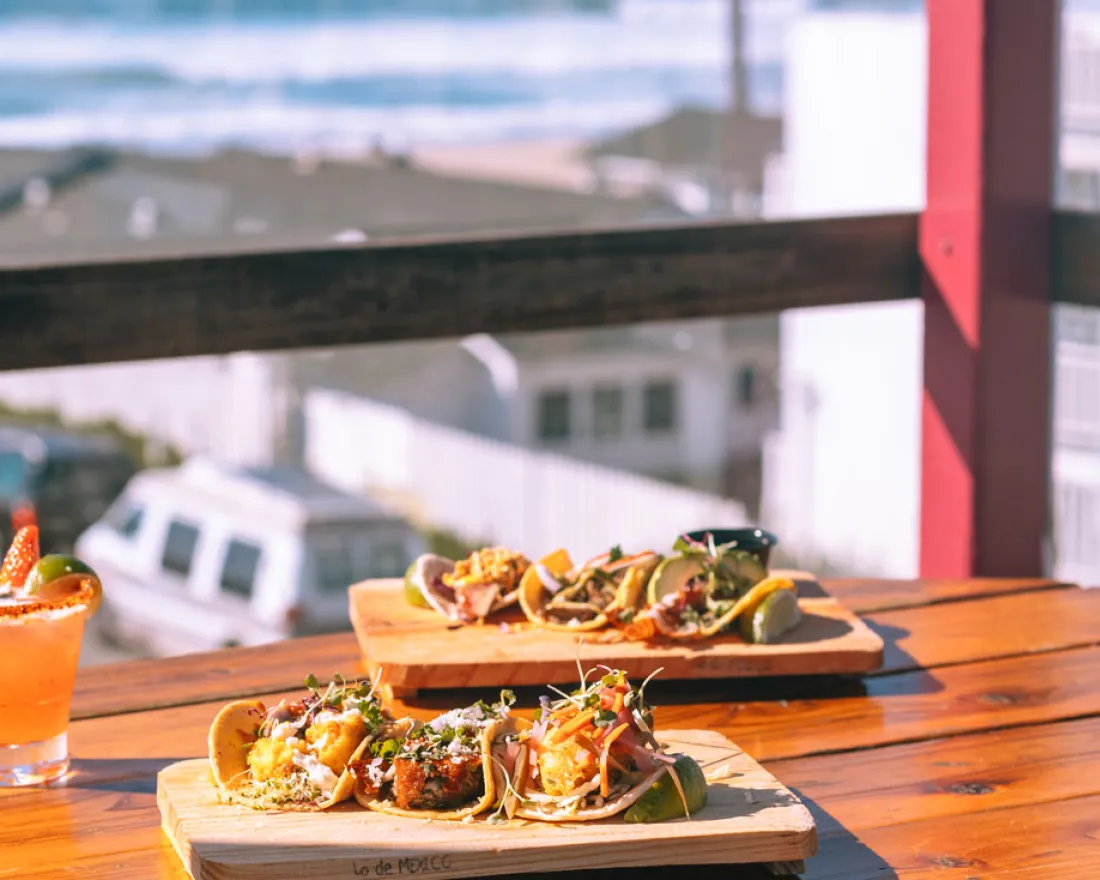 Tacos and cocktail on table looking out a window at San Diego's beach in front