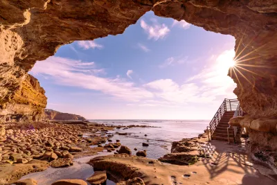 View from inside a rocky seaside cave in Point Loma looking out to the ocean, with a staircase on the right and sunlight streaming through the entrance.