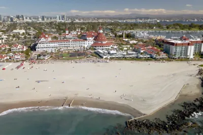 Aerial of Coronado Beach with the Hotel Del Coronado, Coronado Bay Bridge, and San Diego Skyline in the Background.