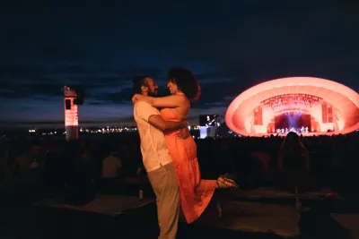 A couple dancing to the music at the Rady Shell at night with San Diego's skyline in the back ground.
