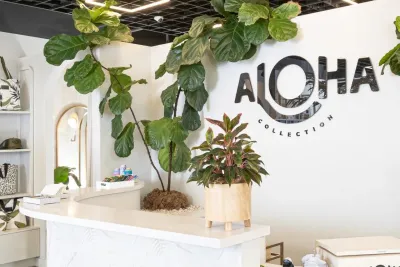 A modern retail store interior at Aloha in Encinitas near San Diego, California, with a white reception desk, green potted plants, and a large "ALOHA COLLECTION" logo on the wall.