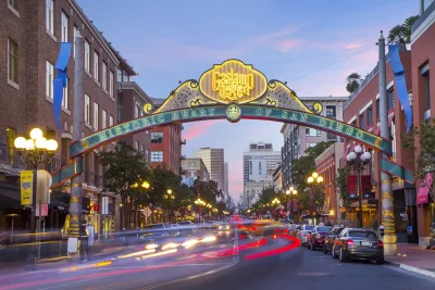 The entrance arch to San Diego’s Gaslamp Quarter is shown over a busy street with blurred car lights and historic buildings at dusk.