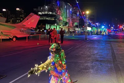 A figure draped in Christmas lights crouches on the deck of the USS Midway Museum during the Jingle Jets holiday event in beautiful San Diego.