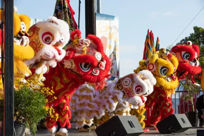 Performers in colorful lion costumes participate in a traditional lion dance on an outdoor stage, with decorations and plants nearby.