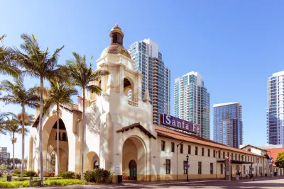 Historic Santa Fe Depot with Spanish-style architecture in front of modern high-rise buildings and palm trees under a clear blue sky.