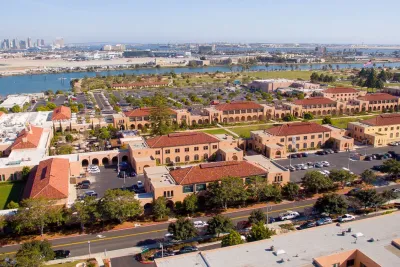 An aerial view of Liberty Station in San Diego, CA, showing red-tiled roofs, broad green lawns and blue waters under sunny skies.