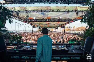 A DJ standing behind his booth on stage as a crowd of people listen to his set in San Diego