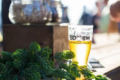 A beer in a San Diego Beer Week pint glass sitting on a table with the sun shining down on it.