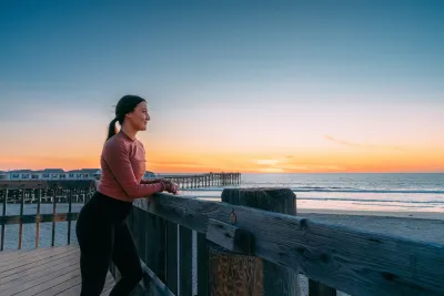A solitary woman stands on a pier looking at a beach near sunset in San Diego.