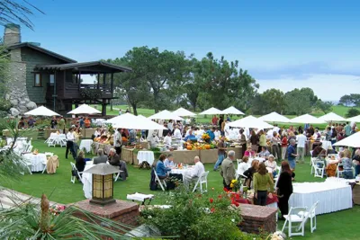 An outdoor shot of multiple people sitting at circle tables with umbrellas as people enjoy the Celebrate the Craft event in La Jolla in San Diego