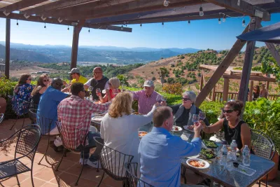 Group meeting taking place on an outdoor patio in San Diego's North Inland area, with attendees seated around a table enjoying food and conversation while overlooking rolling hills and a scenic valley.