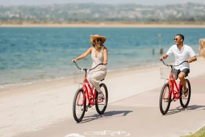A man and woman ride red bicycles along a Mission Bay's sandy beach by the water.