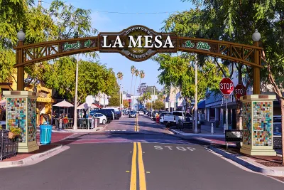 Colorful archway reading "LA MESA" over a tree-lined street with shops and palm trees.