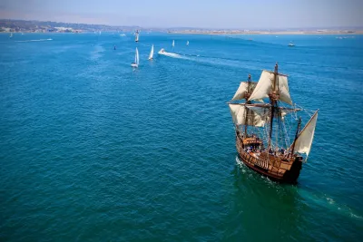 San Salvador wooden sailing ship replica with white sails navigates through a turquoise sea, with smaller boats nearby.