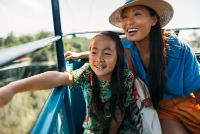 A woman and a girl smile joyfully while riding a cable car, overlooking a scenic view at the San Diego Zoo.