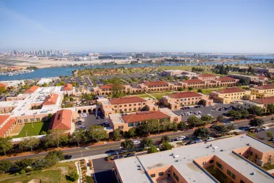 Aerial view of a San Diego's Liberty Station with waterfront, buildings, and green spaces under a clear sky.