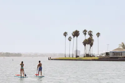 Two people paddleboarding on the calm waters of Mission Bay in San Diego, with palm trees in the background.
