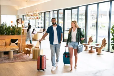 A man and woman walk through a modern hotel lobby at the Town and Country Resort in San Diego, each pulling luggage.