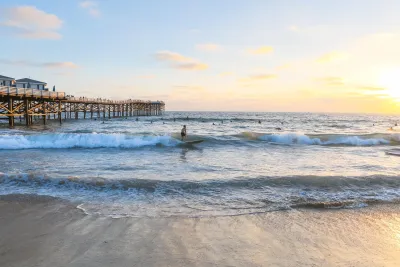 A serene beach scene at sunset with gentle waves and a person near Crystal Pier in San Diego's Pacific Beach.