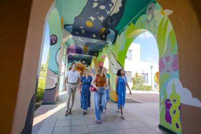 A diverse group of five people walks through a colorful, mural-covered archway at Arts District Liberty Station in San Diego.