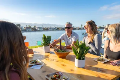 Group of friends laughing and enjoying a meal by the water on a sunny day in San Diego.