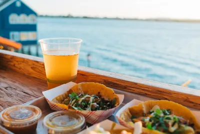 Two taco bowls with toppings, sauces, and a beer, set against a waterfront view in San Diego.