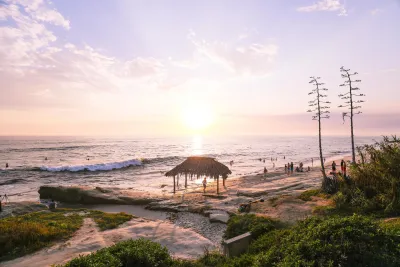 Sunset over the Windansea Beach in San Diego with a straw hut and people enjoying the waves.