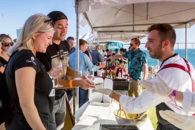 A food vendor serves dishes to two smiling guests at a bustling outdoor festival in San Diego, CA