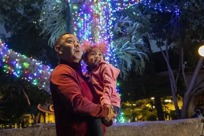 A man holds a girl against a backdrop of a brightly lit tree at night. at the San Diego Zoo 