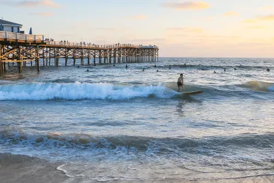 People swimming and surfing alongside Crystal Pier in Pacific Beach, San Diego, CA at sunset