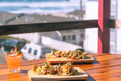 Tacos and cocktail on table looking out a window at San Diego's beach in front