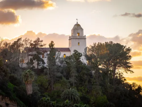A sunset view of Presidio Park in San Diego, with the white adobe museum building in the foreground.