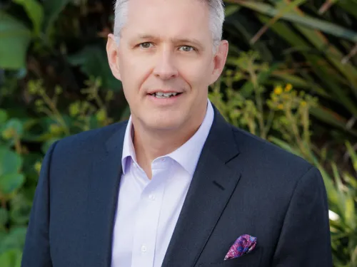 Kavin Schieferdecker, smiling, with short hair wearing a light violet button up and dark navy blazer, outside.