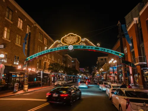 Cars drive under the illuminated Gaslamp Quarter sign on a lively street lined with restaurants and historic buildings in San Diego at night.