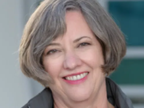 Martha Gilmer with short gray hair and a gray jacket smiles at the camera in an outdoor setting.