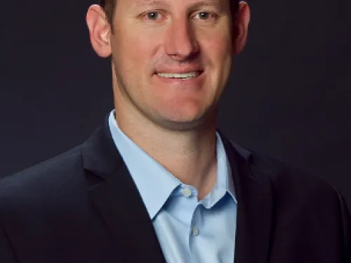 Craig Martin wearing a light blue undershirt with a dark suit, smiling.
