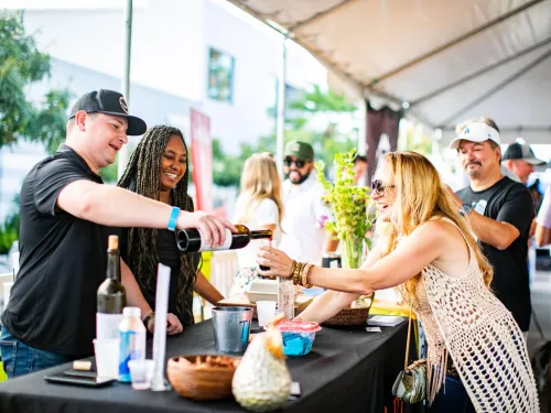 two people getting wine poured into their glass at the La Jolla Wine and Food Festival in San Diego on a sunny day.