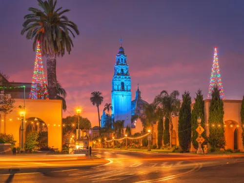 Two Large Christmas trees adorn the rooftops of historic Balboa Park Buildings with the California Down and Tower of the Museum of Us in the background