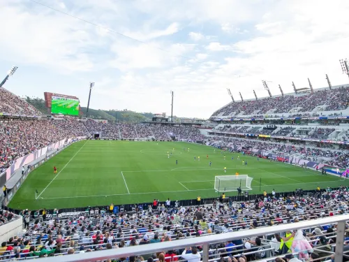 A large stadium filled with spectators watching a soccer match in progress on a clear day.