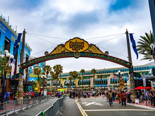 A large archway reading "Historic Heart of San Diego" stands over a busy street filled with people, with palm trees and buildings visible in the background, in San Diego's historic Gaslamp Quarter.