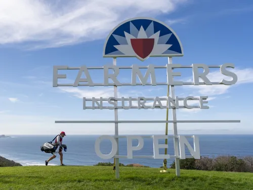 Farmers Insurance Open sign with a golfer walking behind it and the Pacific Ocean in the background