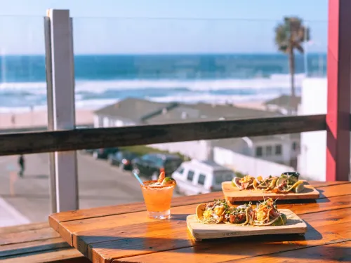 Plates of food and cocktails on a seaside patio overlooking Pacific Beach, capturing the bars and nightlife atmosphere in San Diego.